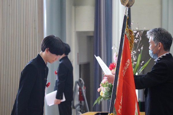 講堂で校長先生から生徒が卒業証書を受け取っている写真