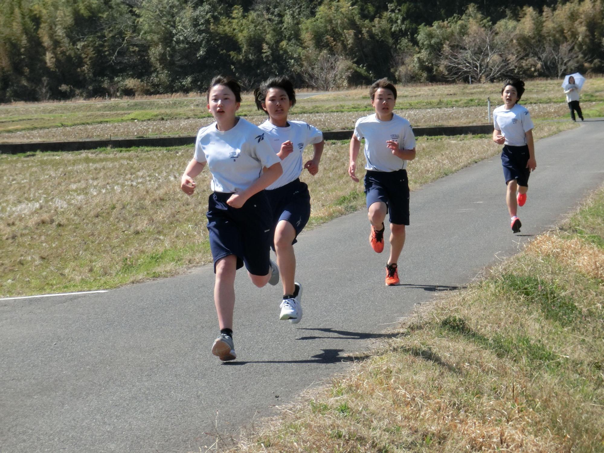 校外の道で女子生徒たちがマラソン大会で走っている写真