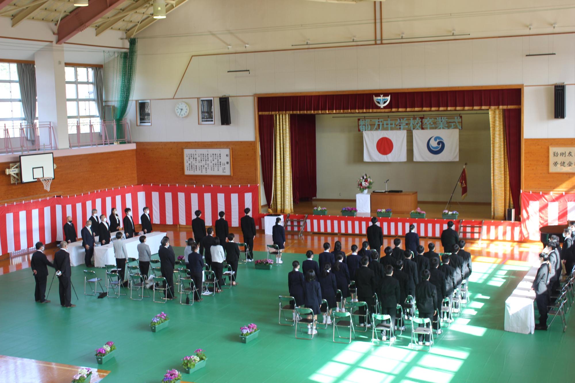 体育館で中学校の卒業式が行われ全員起立している写真