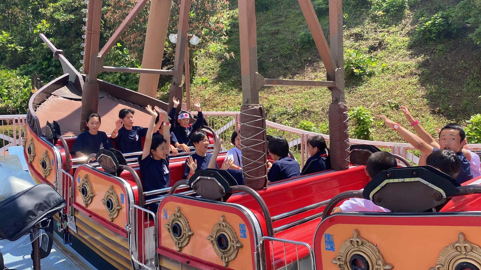 遊園地でバイキングに乗って両手を挙げて楽しむ児童の写真