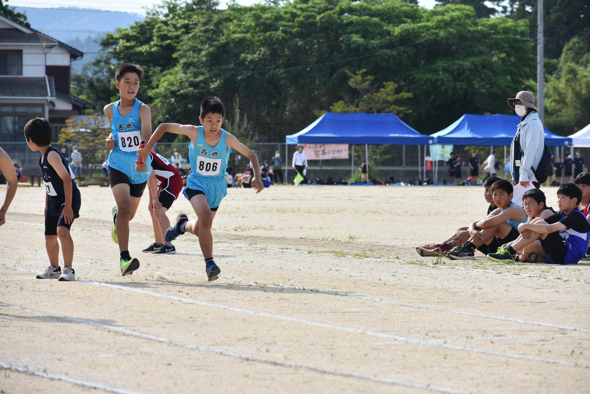 陸上大会でバトンを渡す児童の写真