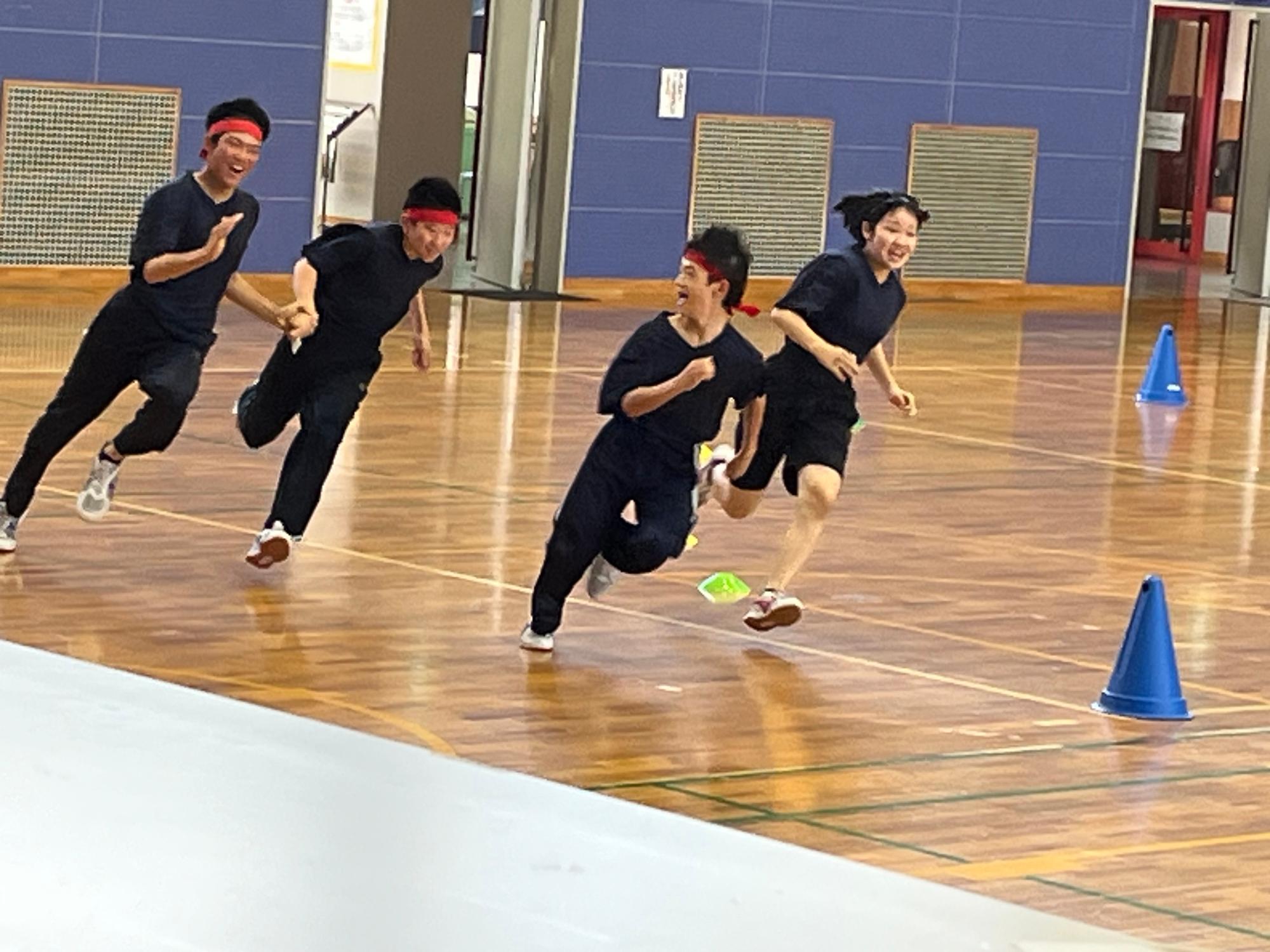 体育館で赤いはちまきをつけた生徒たちがリレーで走っている写真