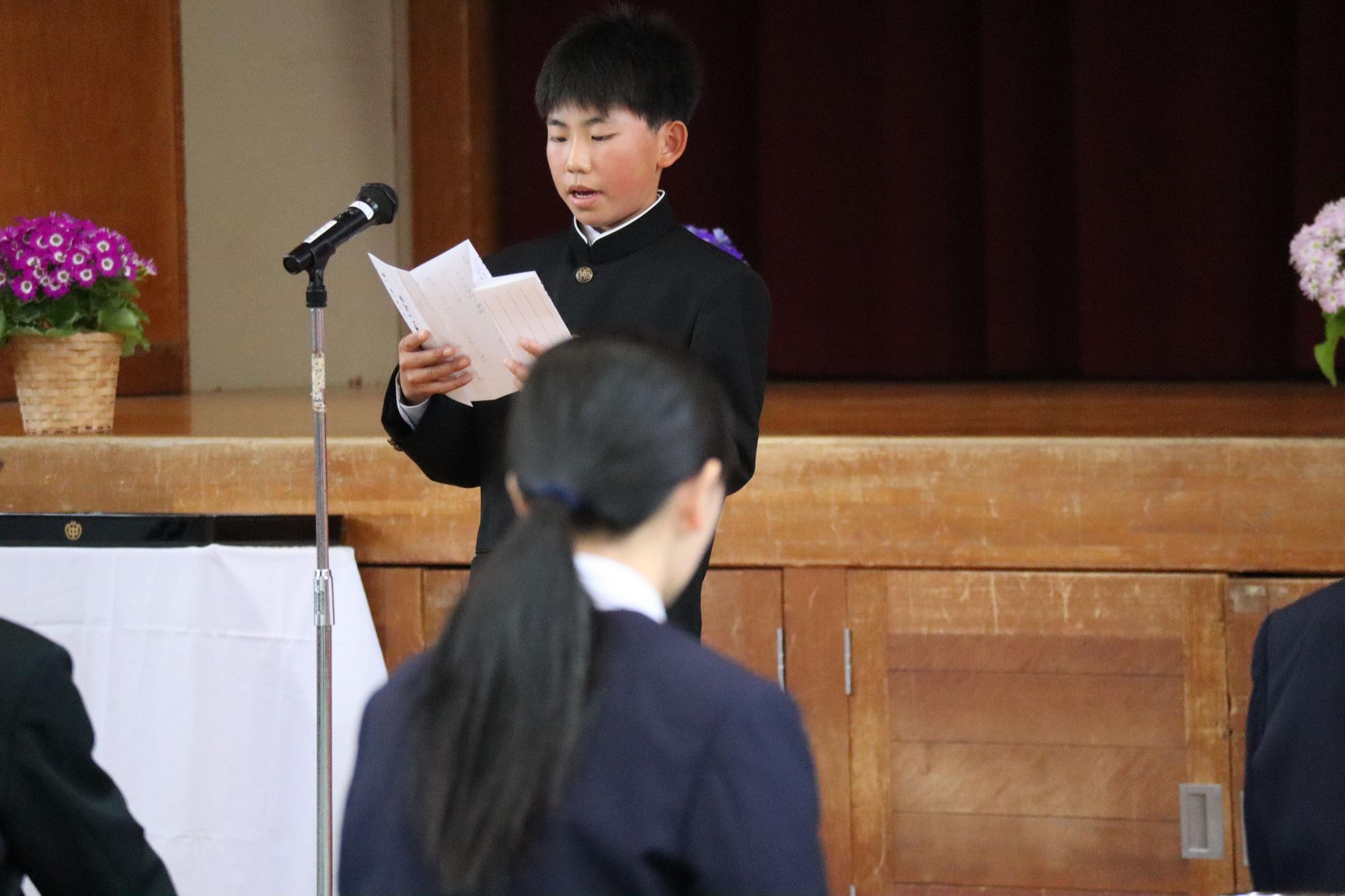 壇上のマイクの前で男子生徒が誓いの言葉を述べている写真
