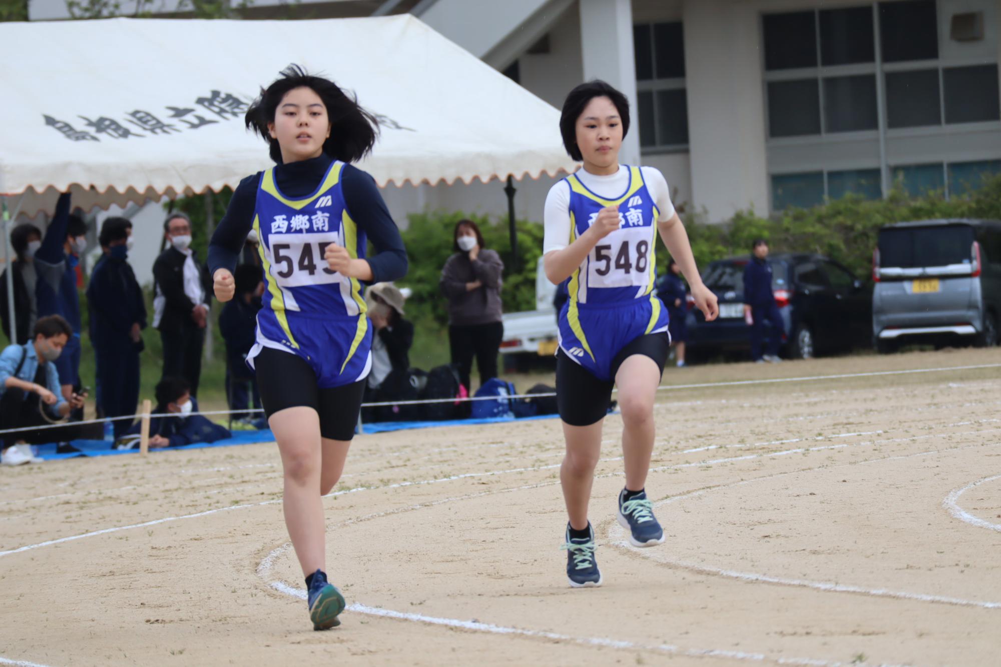 陸上競技大会で女子生徒二人がトラックを走っている写真