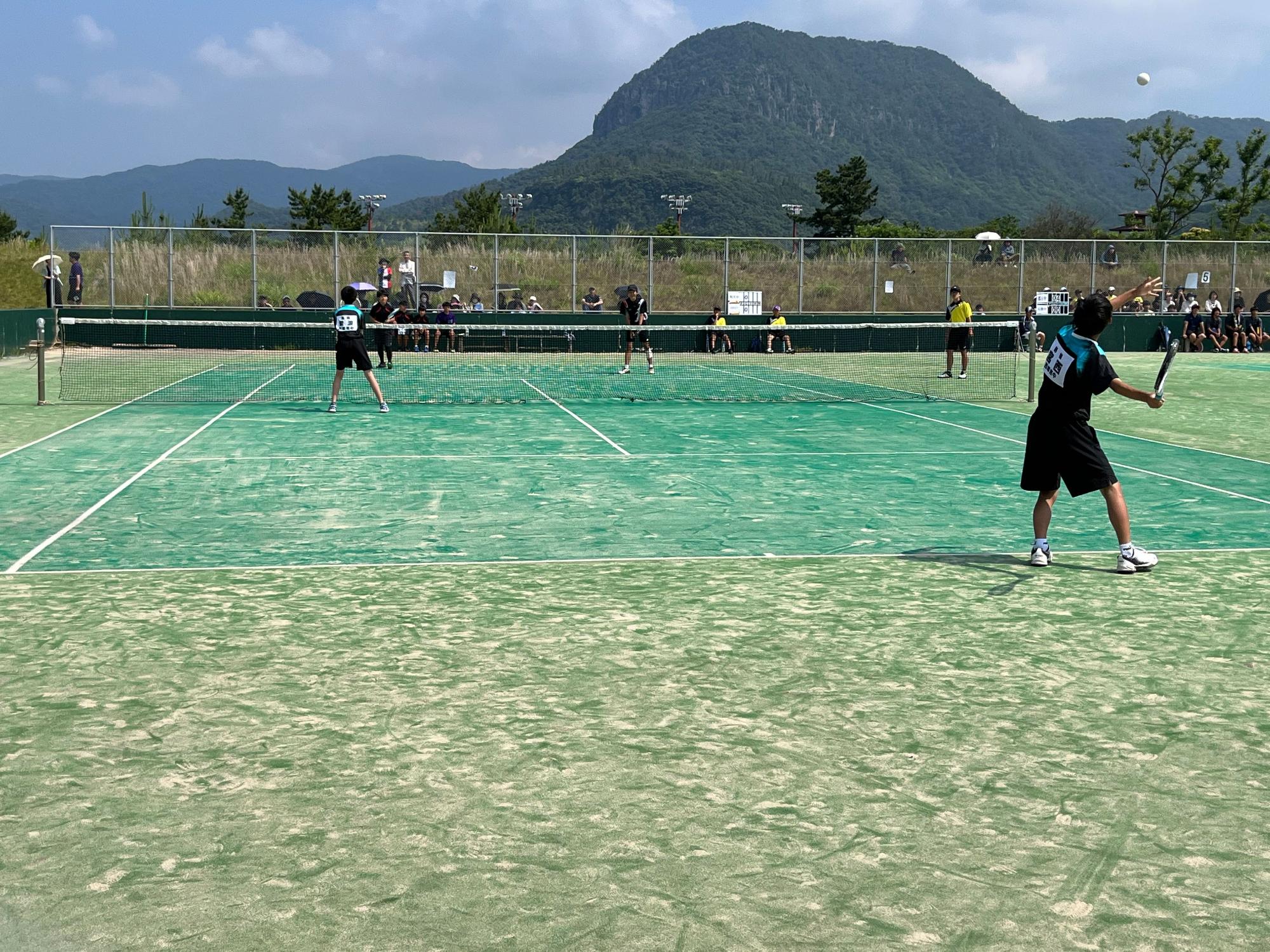 屋外コートで男子生徒がソフトテニスの試合をしている写真