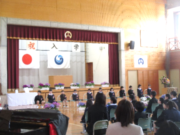 体育館で新入生がステージ前に並ぶ入学式の写真