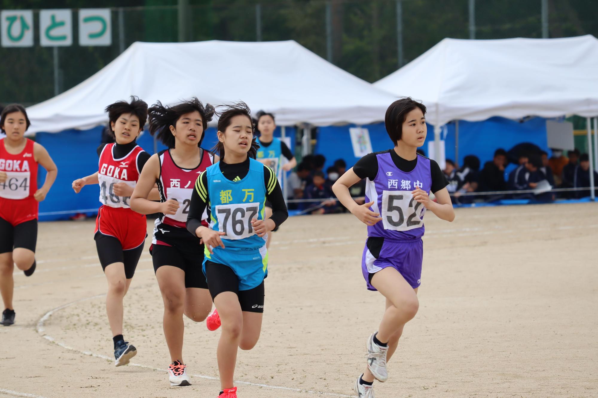 陸上大会でカラフルなゼッケンをつけた女子生徒たちが走っている写真