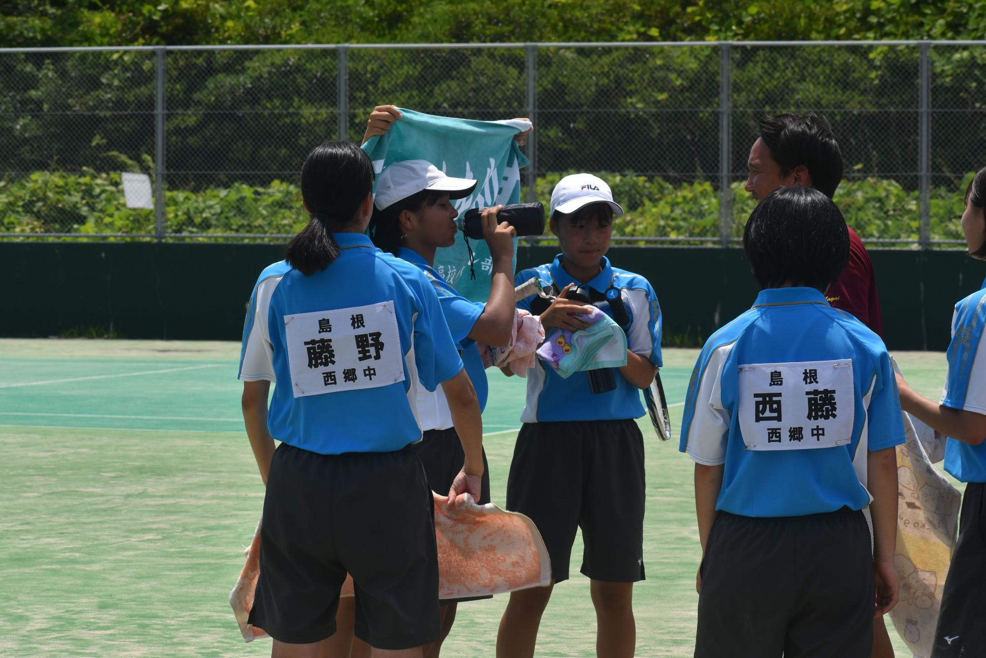 テニスコートで女子ソフトテニス部が休憩や作戦会議をする写真
