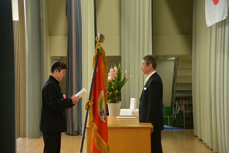 体育館の壇上で新入生の代表が入学の誓いを述べている写真