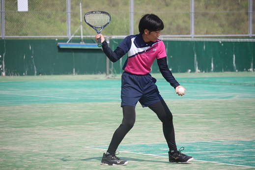 テニスコートで女子生徒が構えてボールを打とうとしている写真