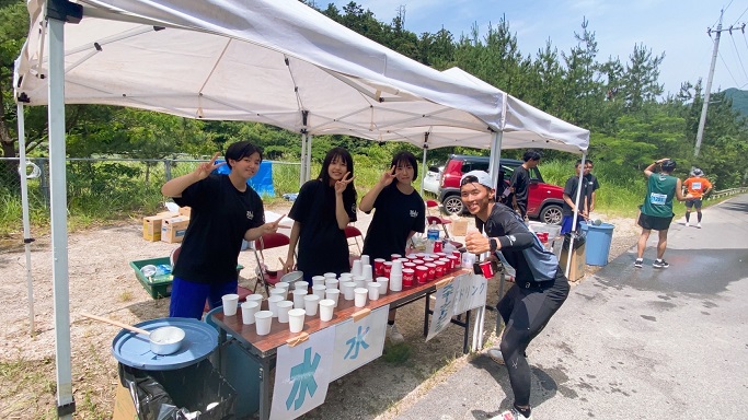 マラソンの給水所で生徒たちが笑顔でランナーを応援している写真