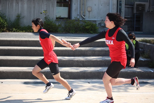 陸上ユニフォームを着た生徒がバトンをつないでリレーしている写真