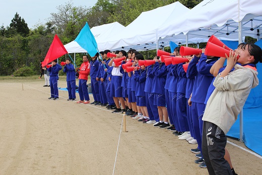 テントの前でジャージを着た生徒がメガホンを使って声援を送っている写真