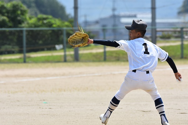 野球場でユニフォーム姿の選手がピッチャーとしてボールを投げている写真