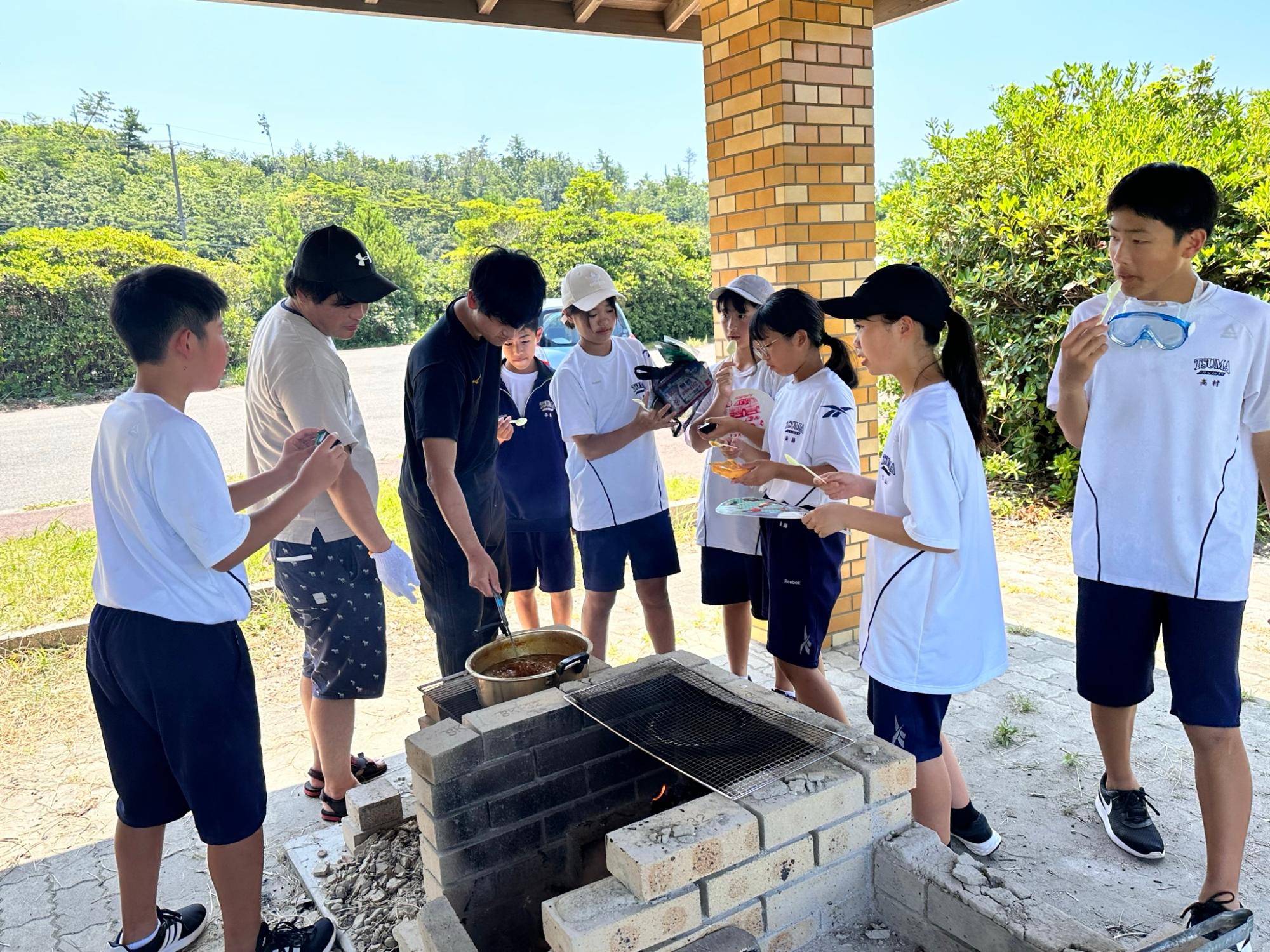屋外のかまどで生徒たちがカレー作りをしている写真