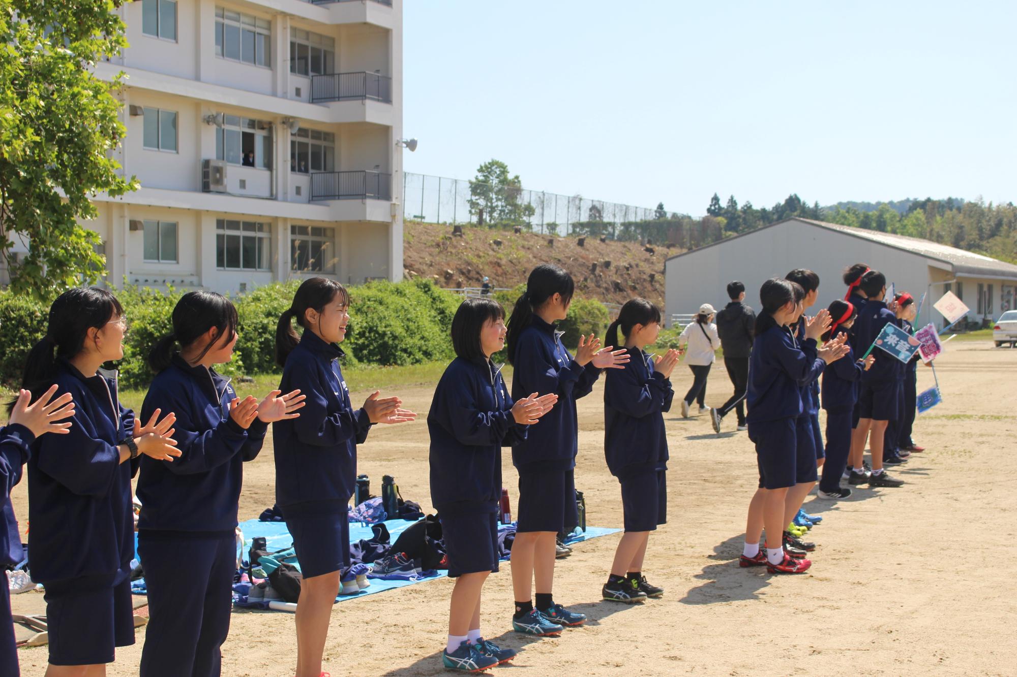 校庭で生徒たちが拍手をして応援している写真