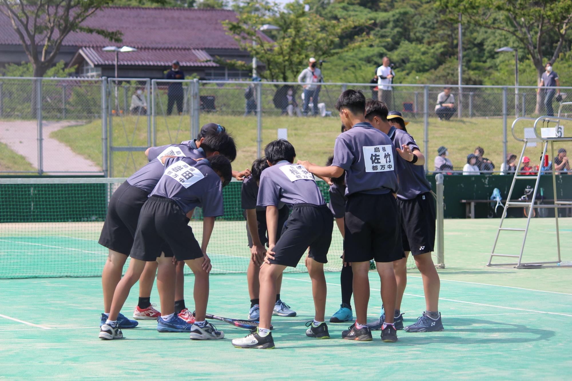 テニスコートで男子生徒たちが円陣を組んで気合を入れている写真