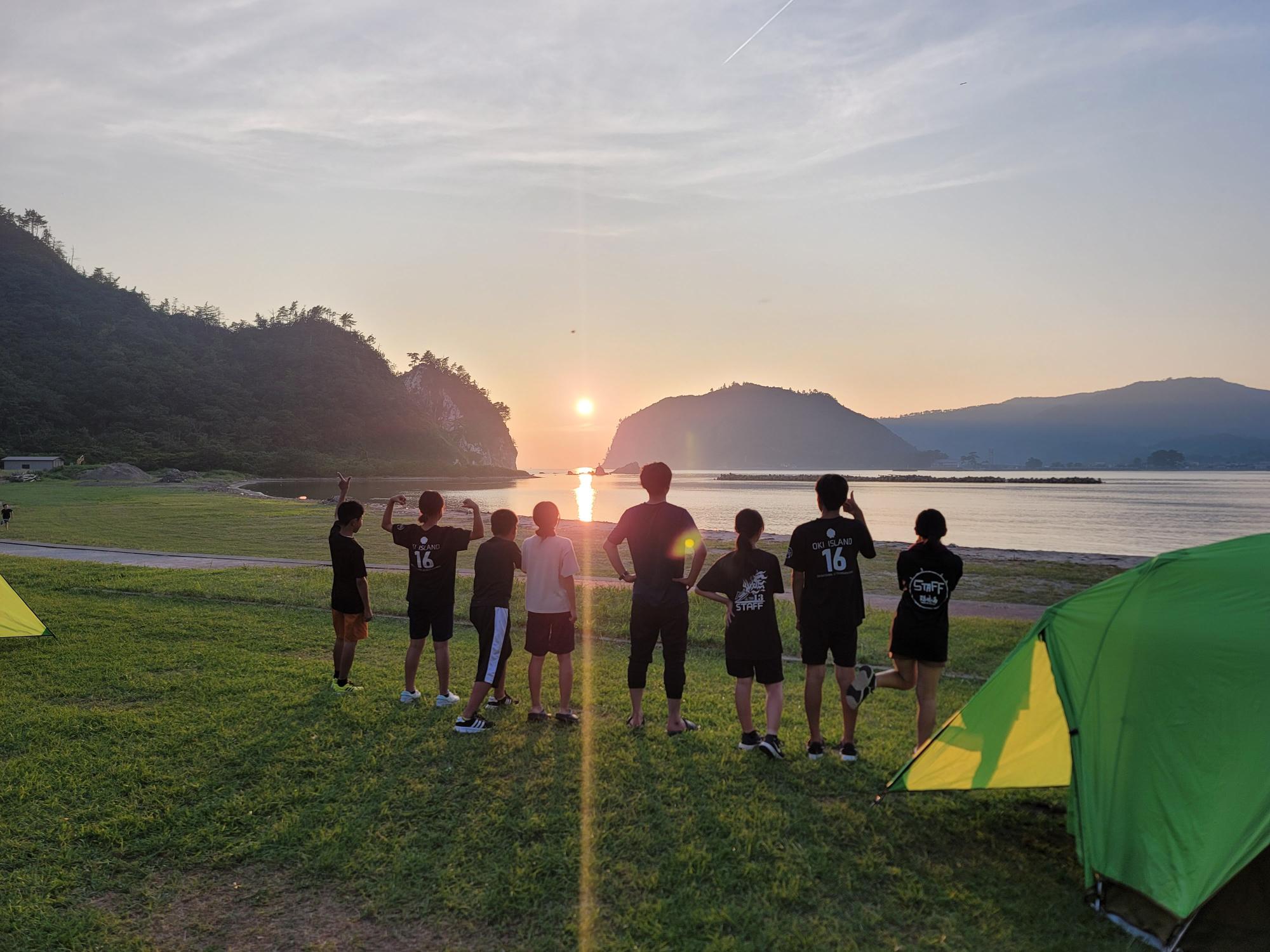 海辺のキャンプ場で生徒たちが夕日を眺めている写真