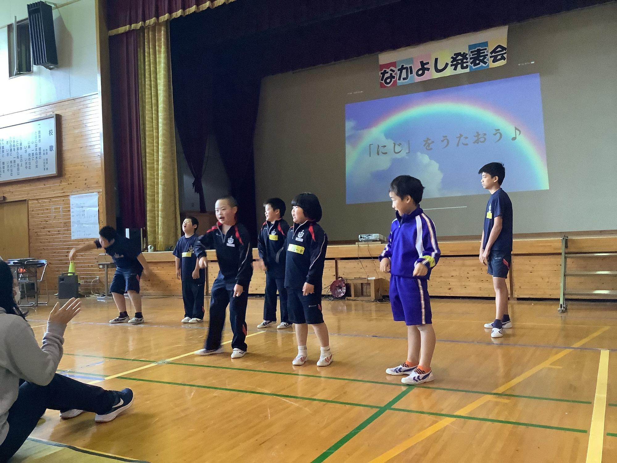 体育館で座っている先生の前でダンスを披露している写真