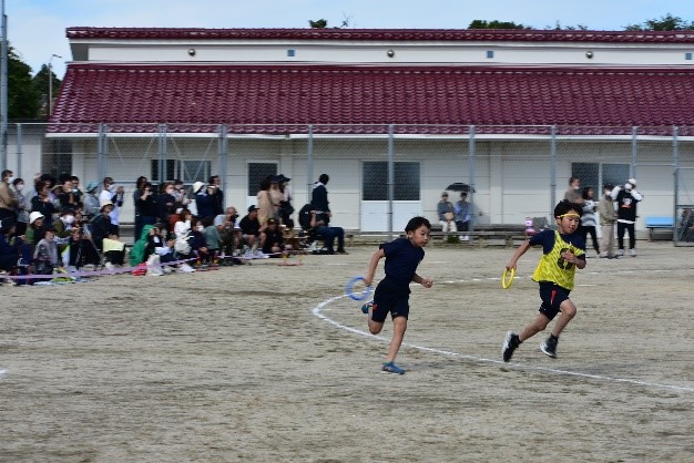 グラウンドで児童がバトンを持ってリレーをしている写真