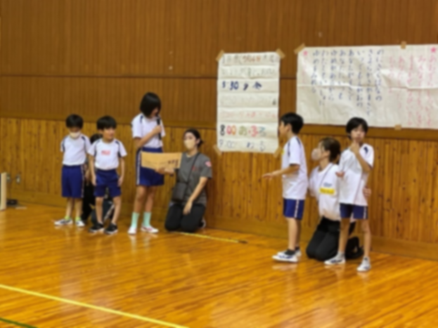 体育館の壁際で司会の児童が発表する様子の写真