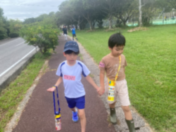 道路脇の遊歩道を手をつないで歩く児童2人の写真