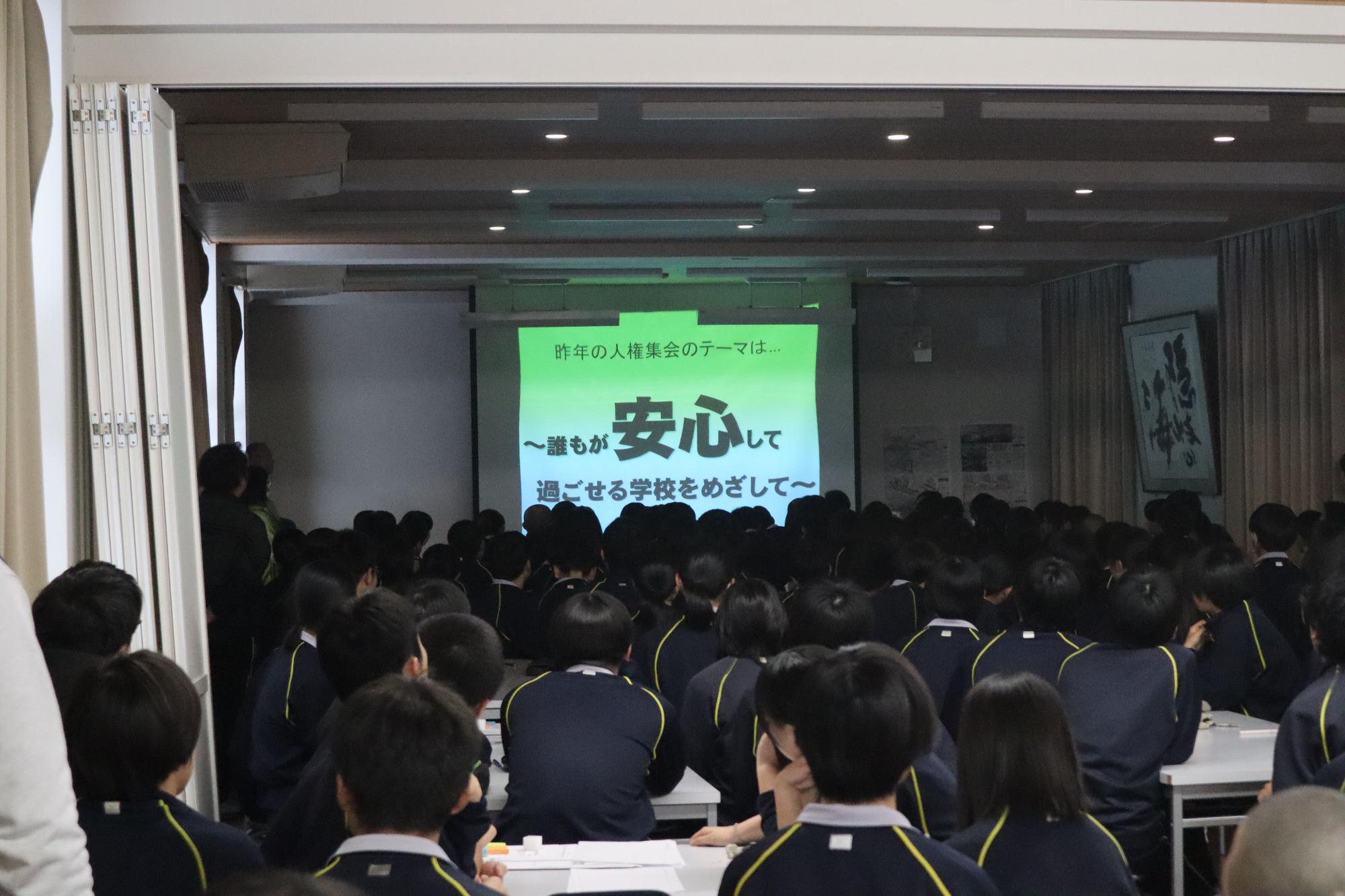 講堂で人権集会のスライドを見ている生徒たちの写真