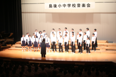 体育館のステージで生徒たちが合唱をしている写真