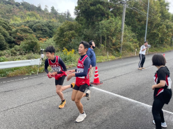 道路沿いで生徒たちが駅伝のたすきをつないでいる写真
