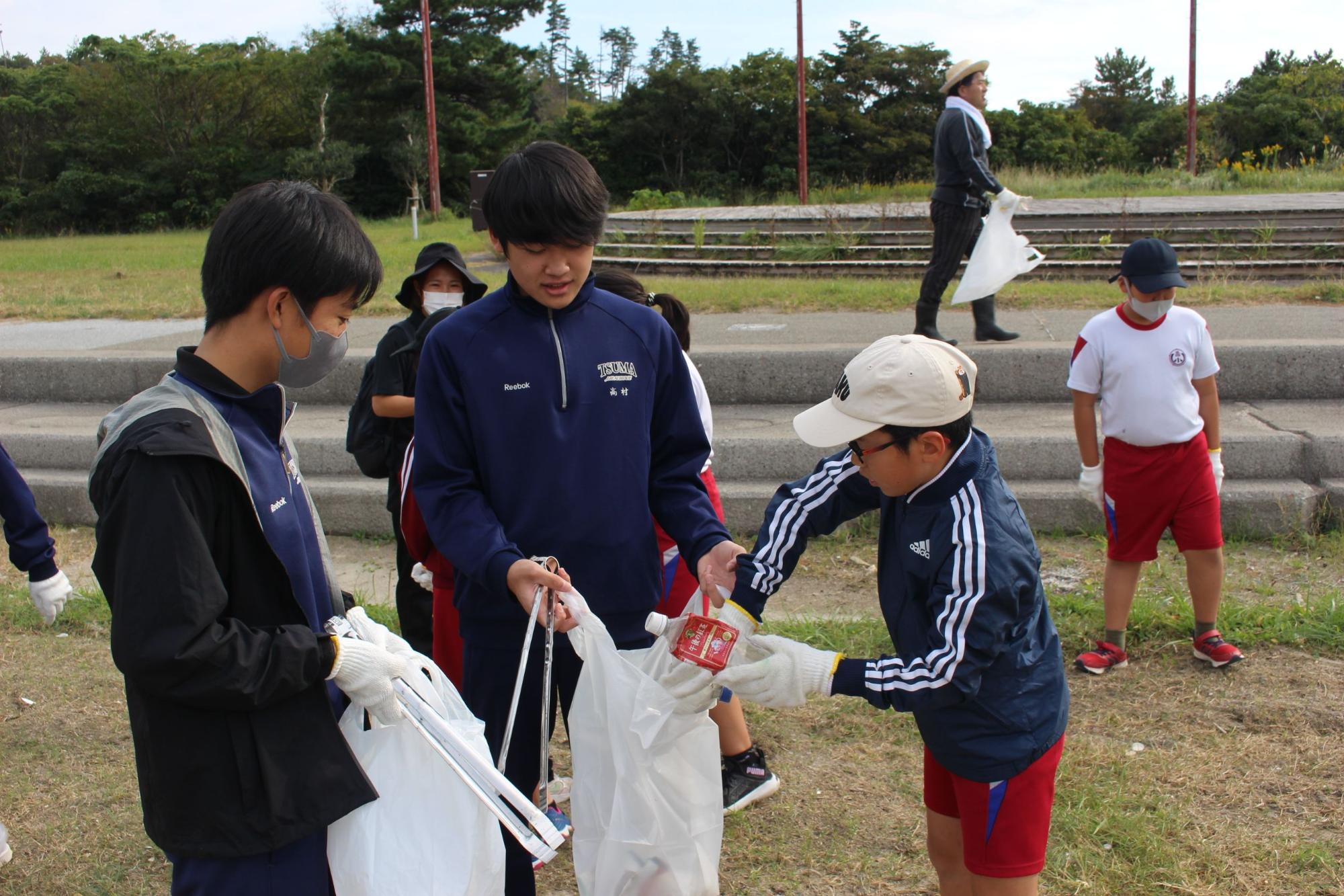 グラウンドで児童と生徒が軍手をして一緒にごみを集めている写真