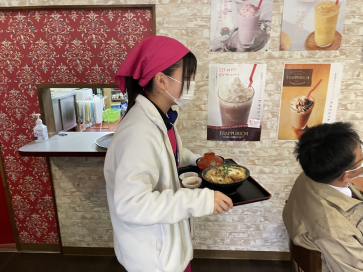 飲食店で生徒が料理を運んで接客している写真