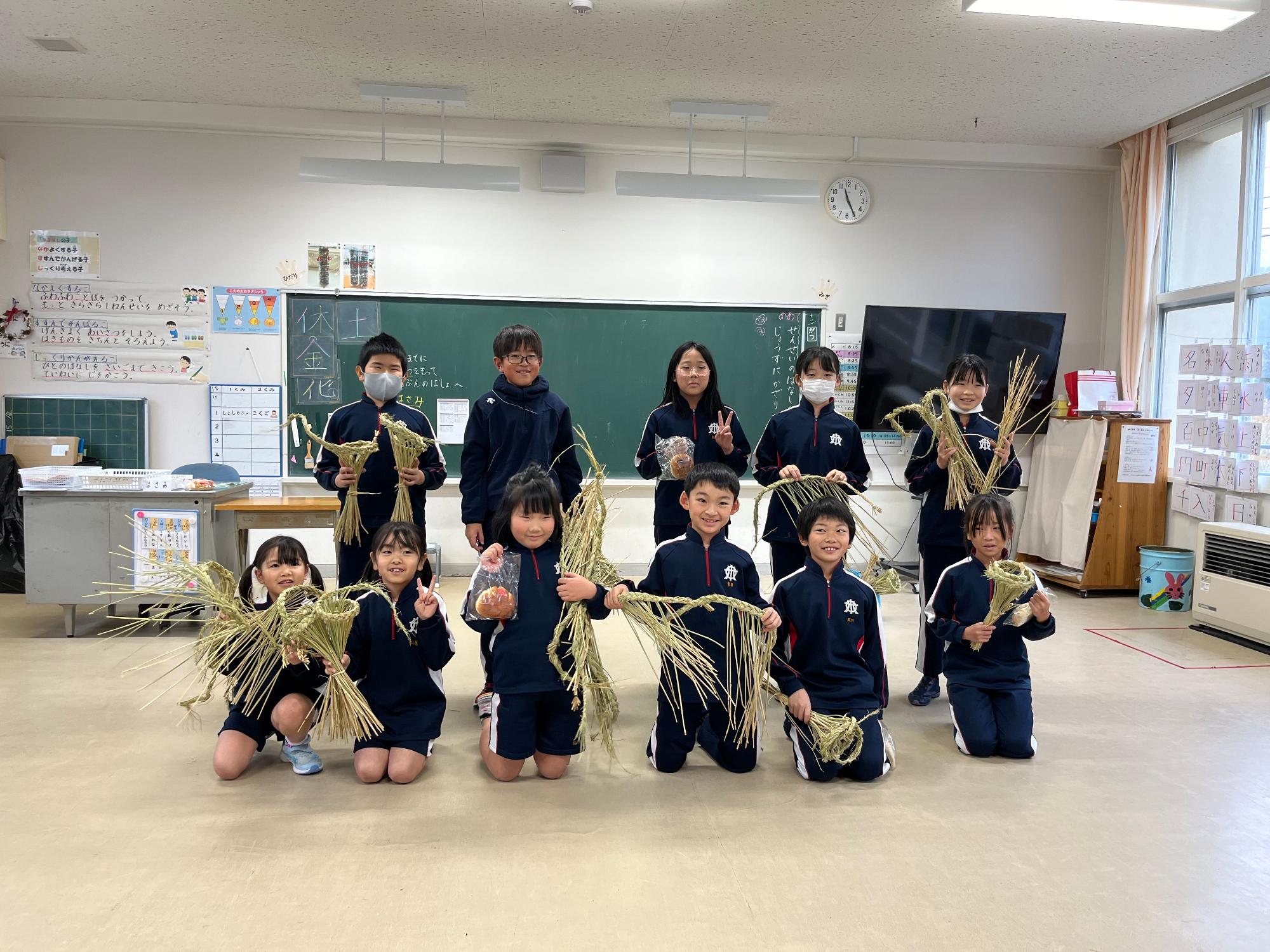 教室でしめ縄を持って二列に並ぶ複数人の児童たちの記念写真