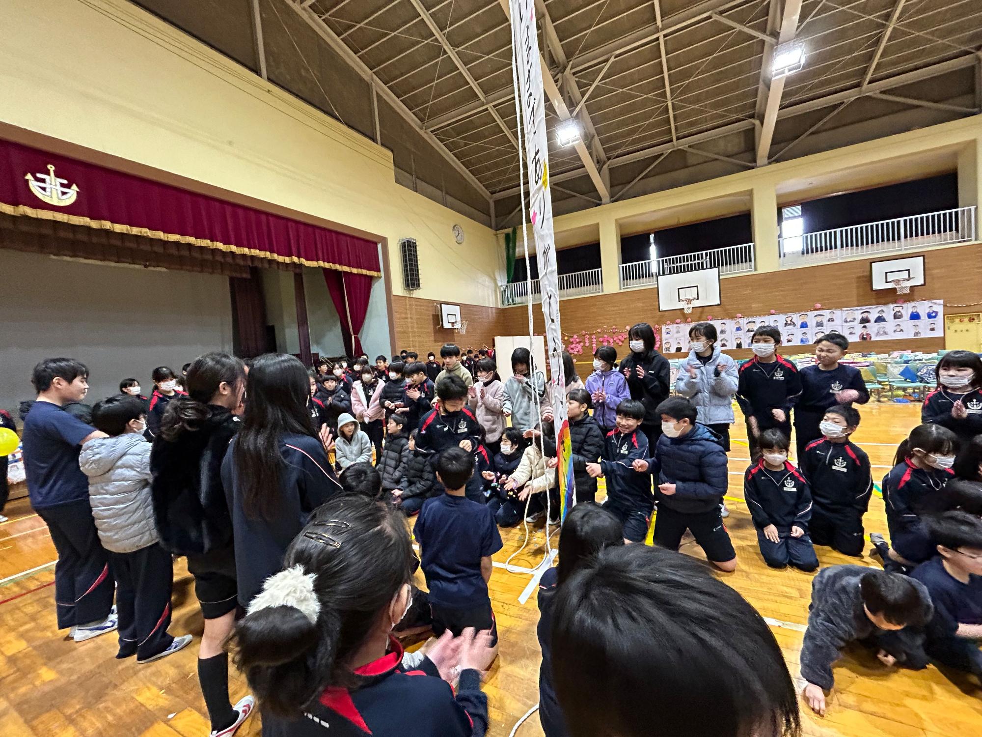 体育館でくす玉を囲んで拍手する児童たちの写真