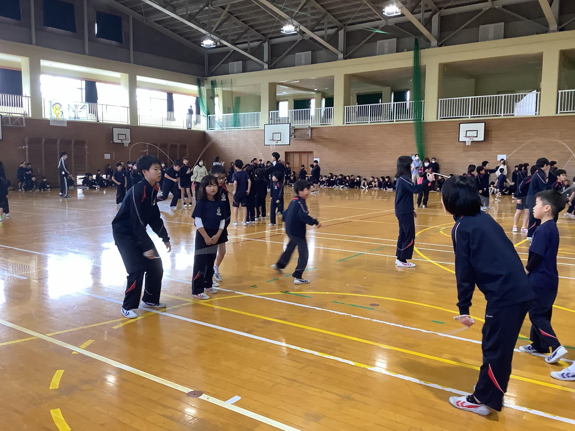 体育館で長縄跳びに挑戦する児童たちの写真