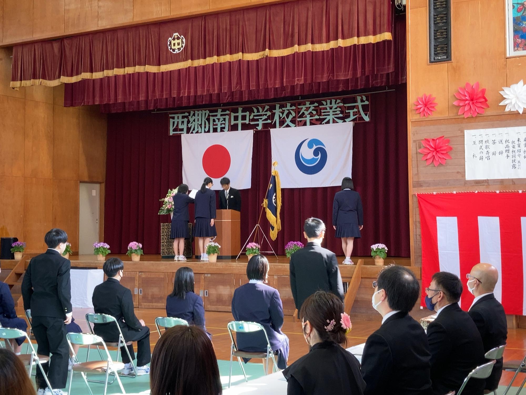 体育館の舞台の上で複数人の生徒が卒業証書を受け取っている写真