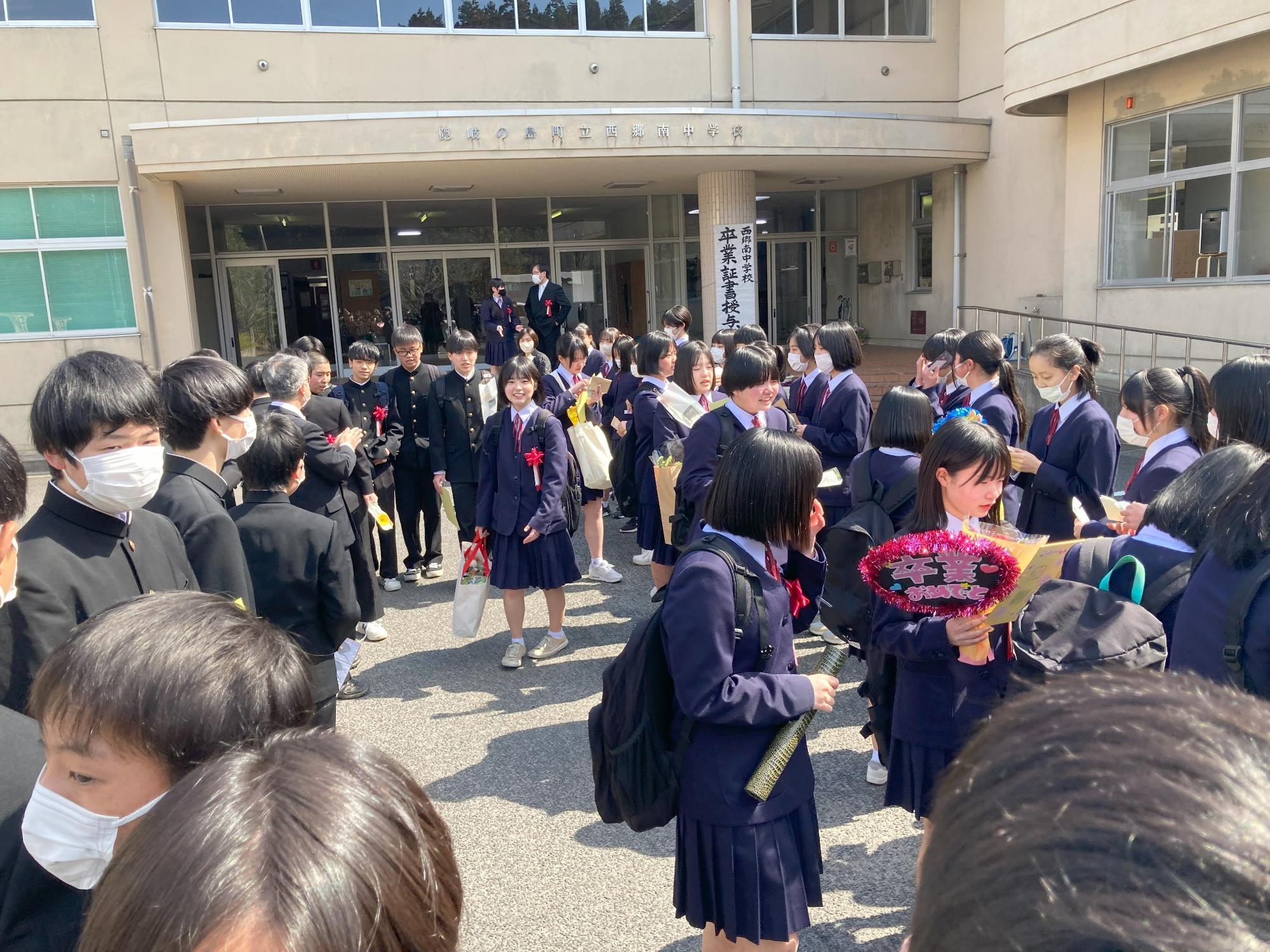 学校の玄関前で数十人の生徒たちが花束を手に集まっている写真