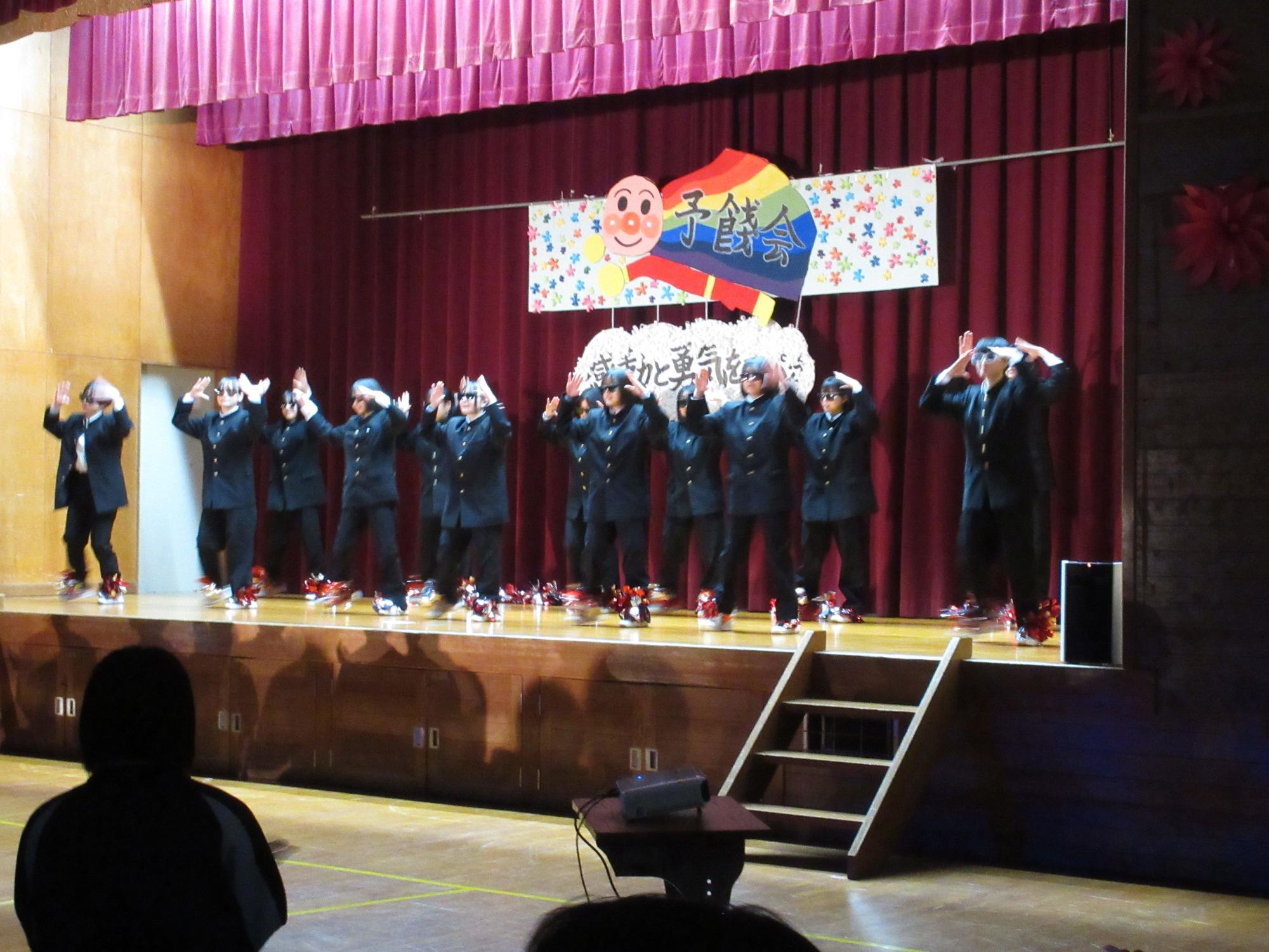 体育館の舞台で制服姿の生徒たちがダンスを披露している写真