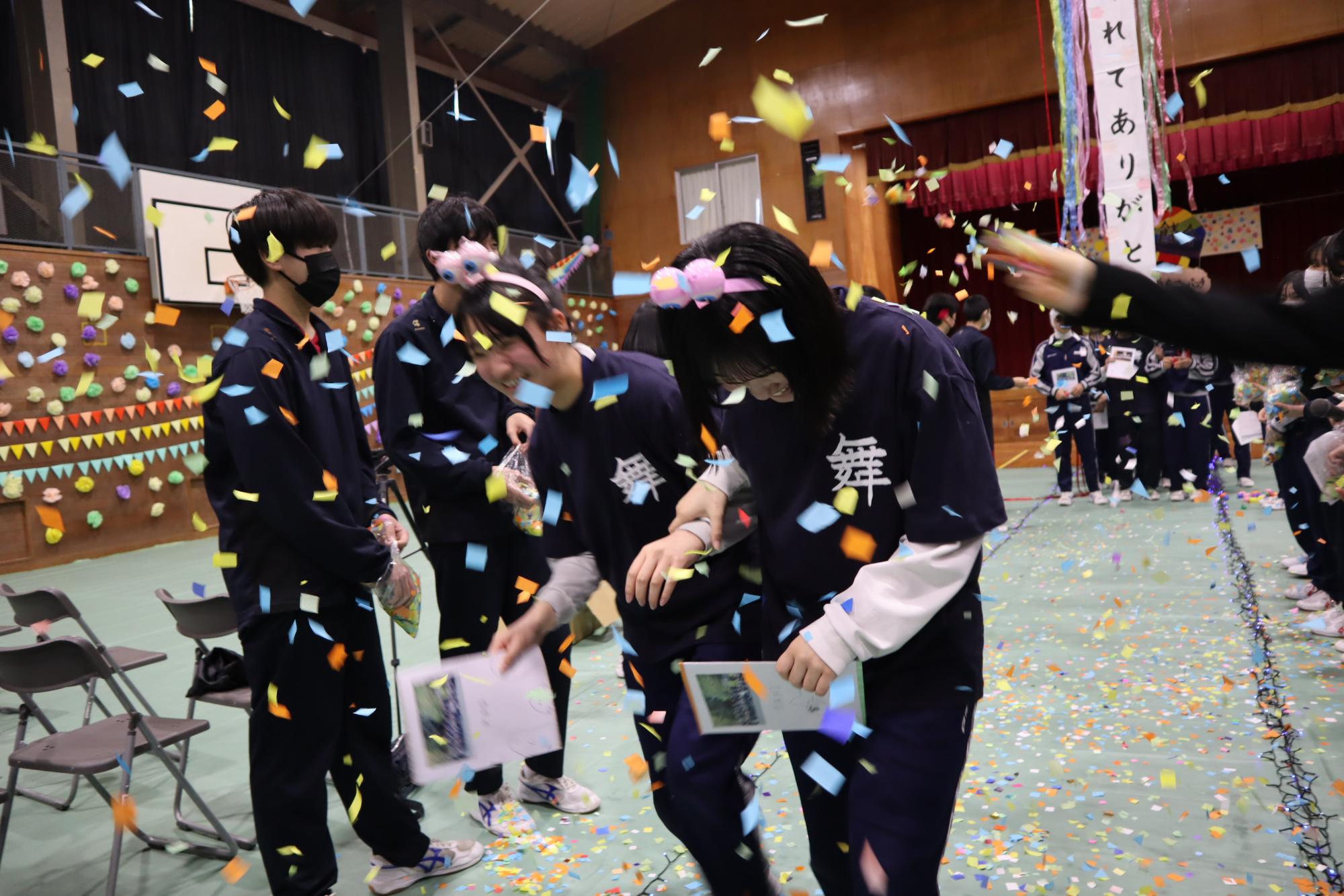 体育館の通路で紙吹雪が舞う中、生徒たちが笑顔で歩いている写真