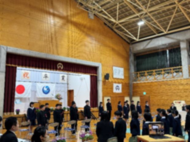 体育館の舞台前で卒業式に臨む児童たちが整列している様子の写真