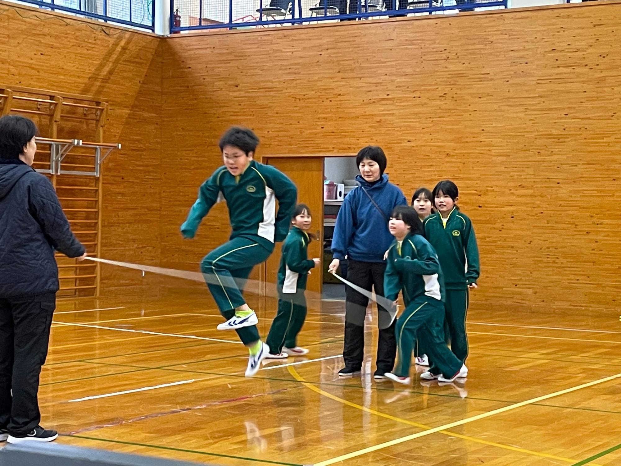 縄を飛ぶ生徒と順番に並ぶ生徒と縄を回す2人の大人が写っている校内なわとび大会の写真