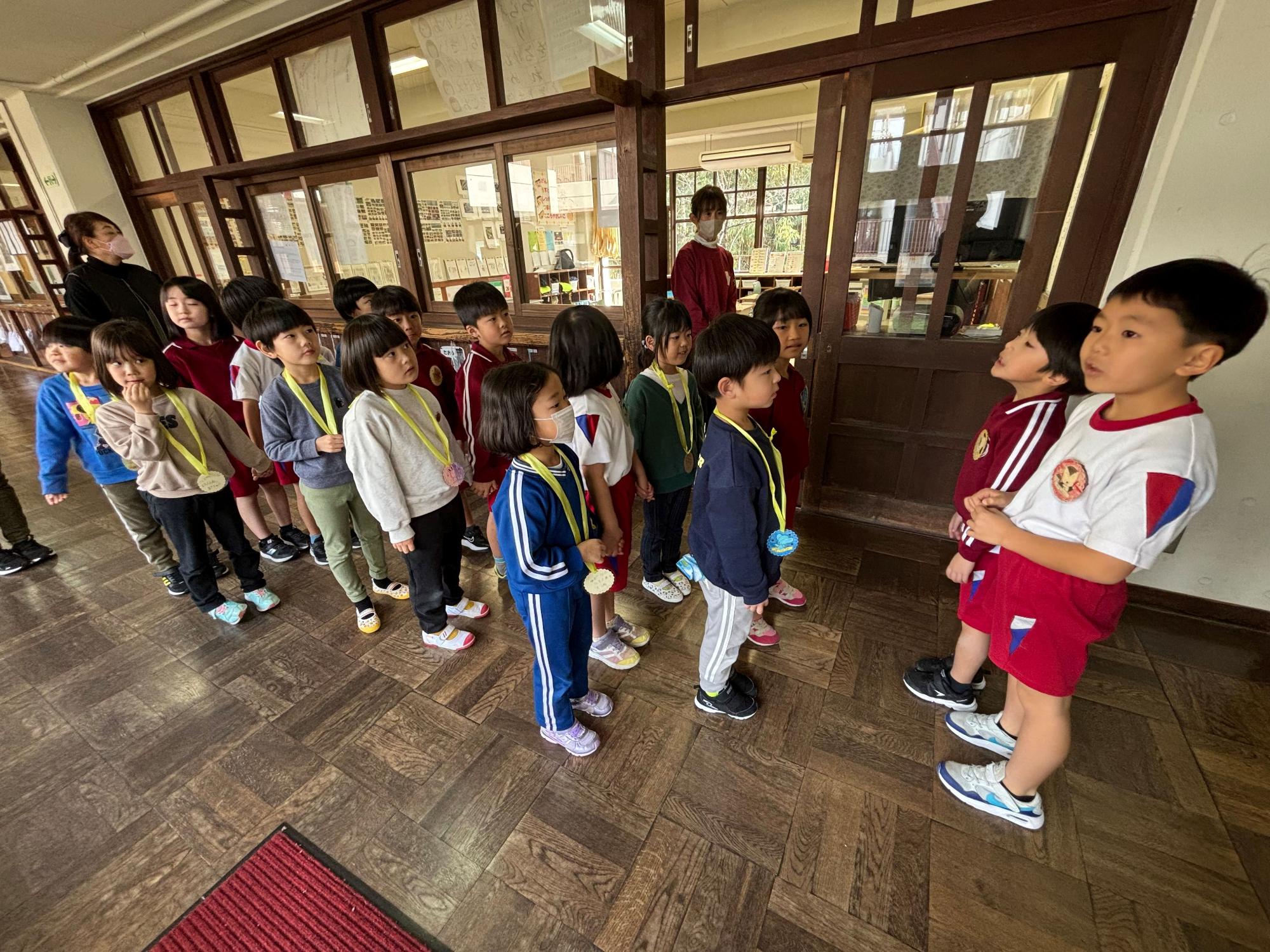 廊下でメダルをかけた児童たちが列になって向かい合っている写真