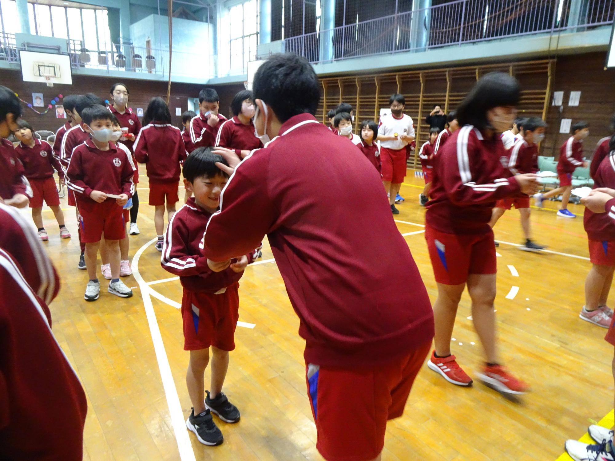 体育館で上級生が下級生にメダルをかけて表彰している写真