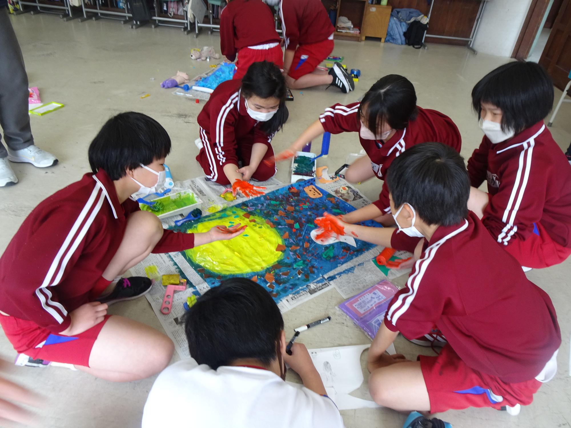 教室で児童たちが絵の具で手形を押しながら共同制作をしている写真