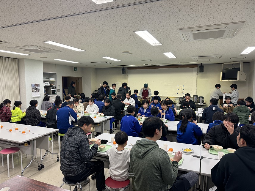 食堂でたくさんの生徒と教職員が一緒に食事をしている写真