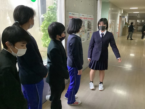 校舎の廊下でマスクを着用した生徒が児童に学校案内をしている写真