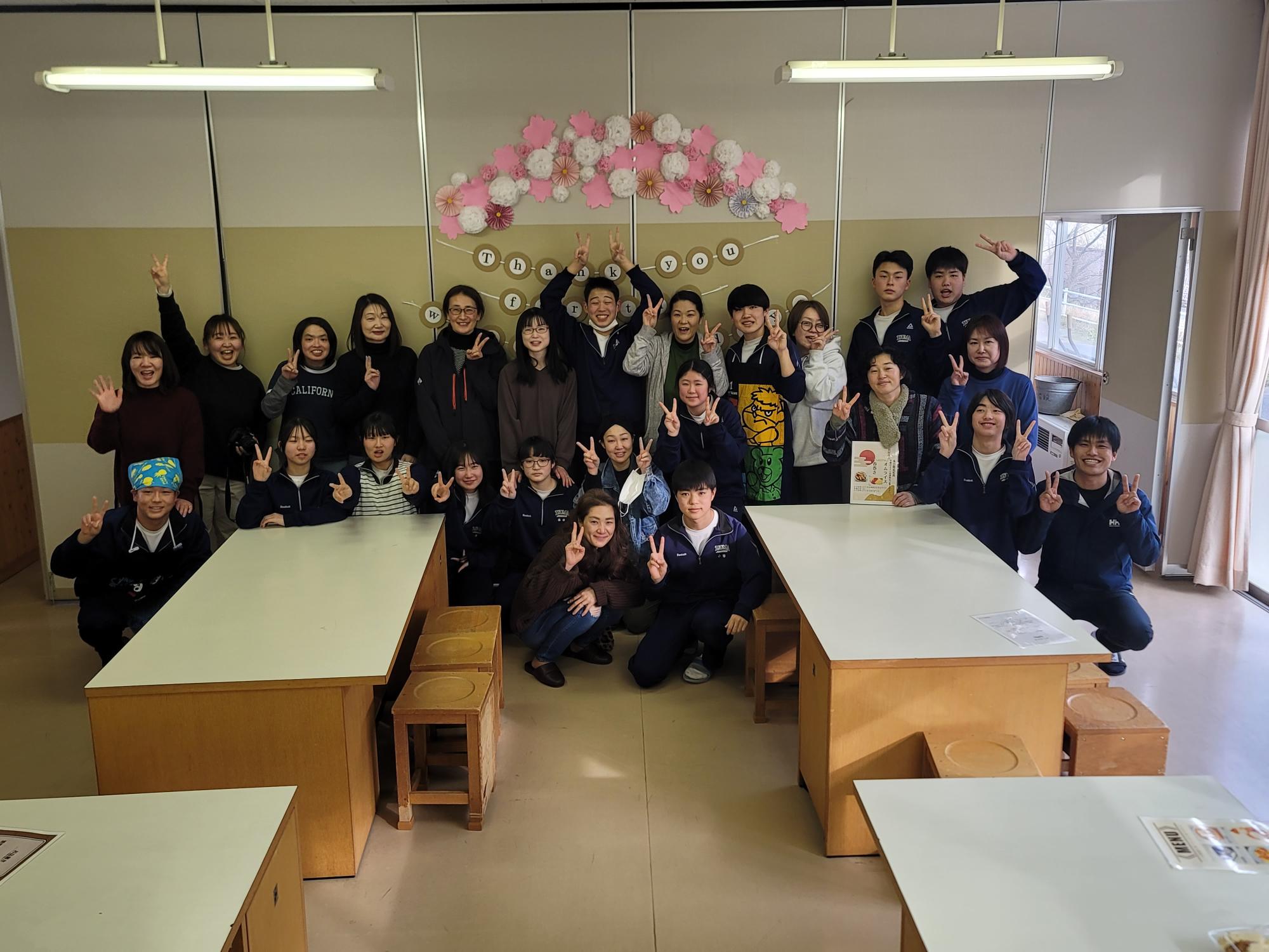 教室で感謝の飾りを背景に生徒と教職員が集合して記念撮影をしている写真