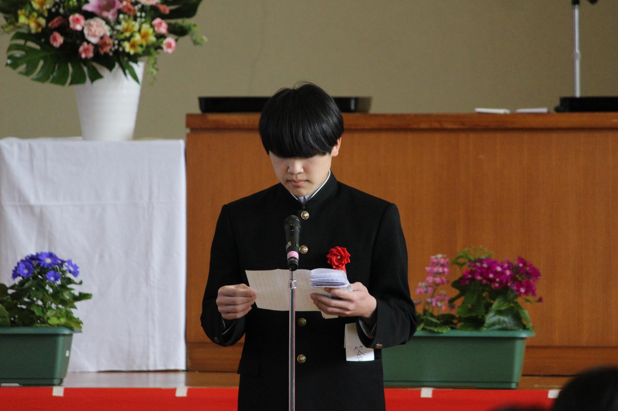 体育館で卒業式の壇上に立ち、答辞を読む男子生徒の写真