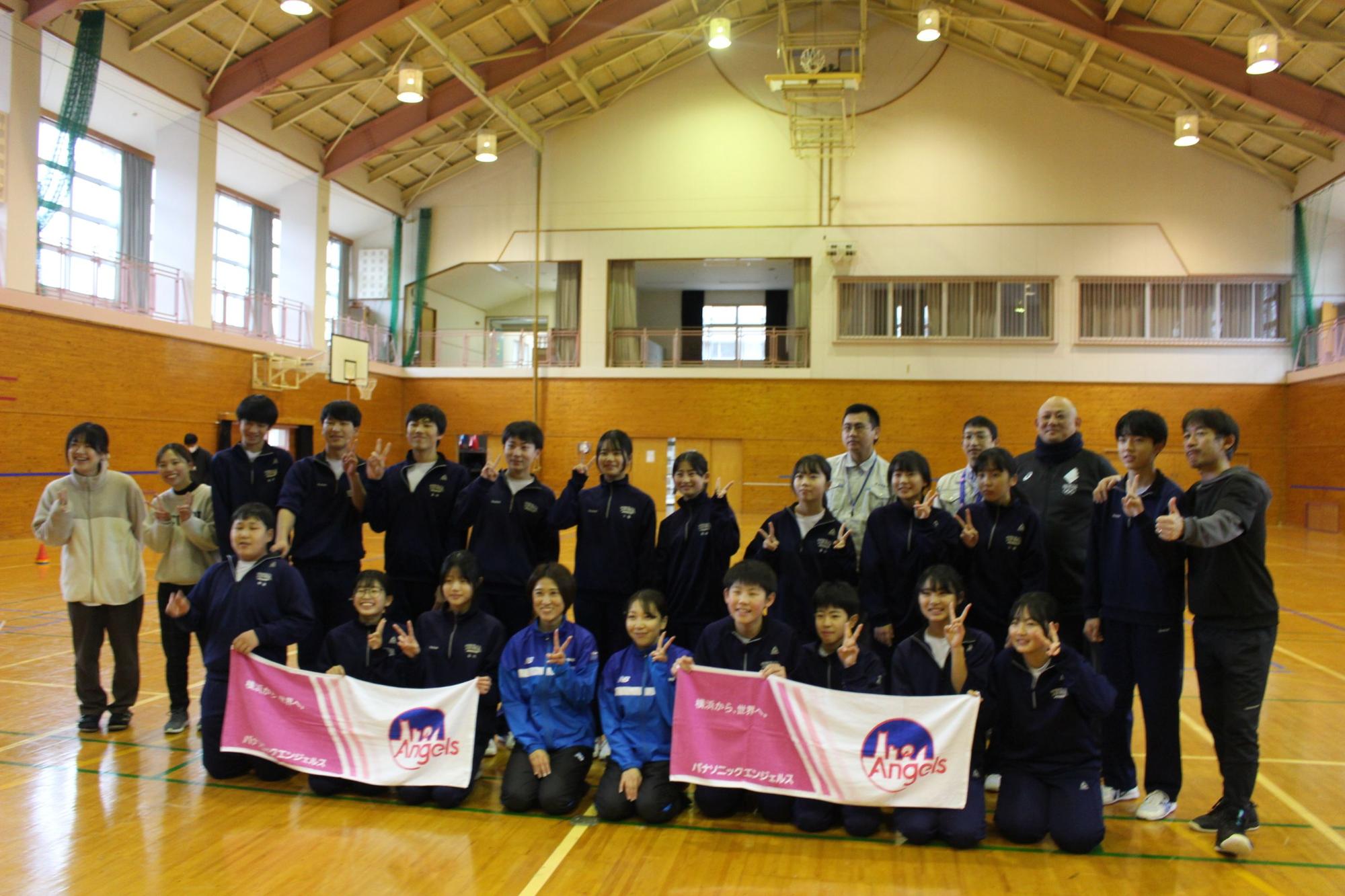 体育館で講師と生徒たちが記念撮影をしている写真