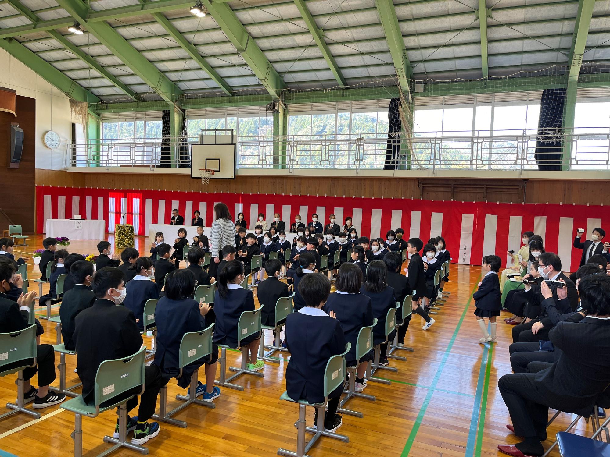 体育館で児童たちが入学式に参加している写真