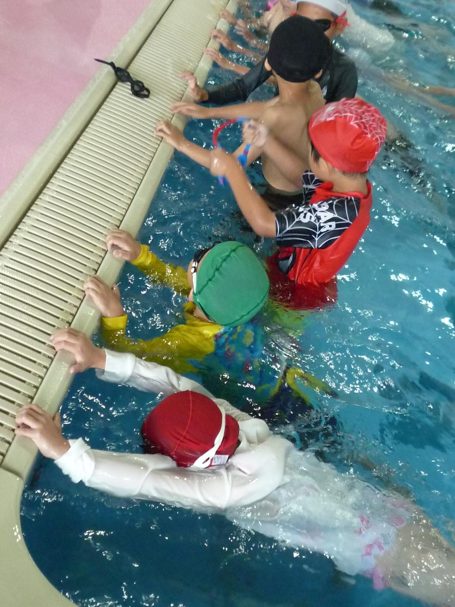 プールで児童たちが壁につかまりながら水泳練習をしている写真